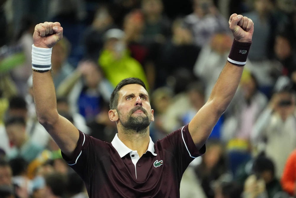 Tennis player in maroon Lacoste polo and wristbands raises both fists in celebration in a crowded stadium at the China Open