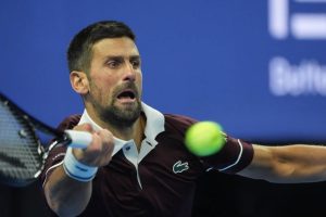 Tennis player in maroon Lacoste polo and white wristbands hitting a forehand on a blue court, ball in motion, at the China Open