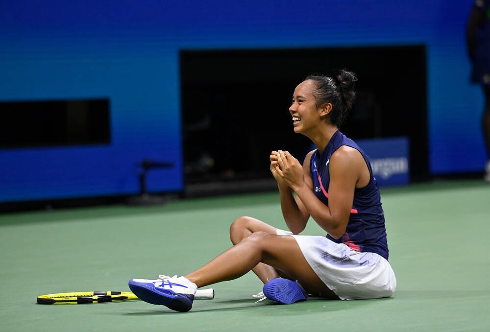 Leylah Fernandez sits on the court in a navy top and white skirt, smiling and clasping her hands in celebration after winning the Singapore Open title.