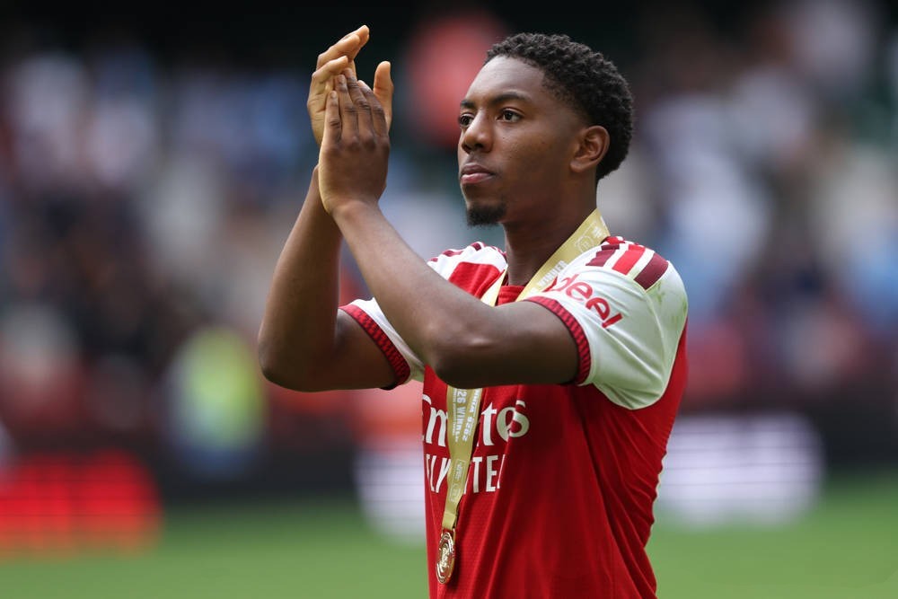 Young footballer in red and white Arsenal kit with a gold medal, applauding fans in a stadium. Likely Myles Lewis-Skelly, Golden Boy finalist.