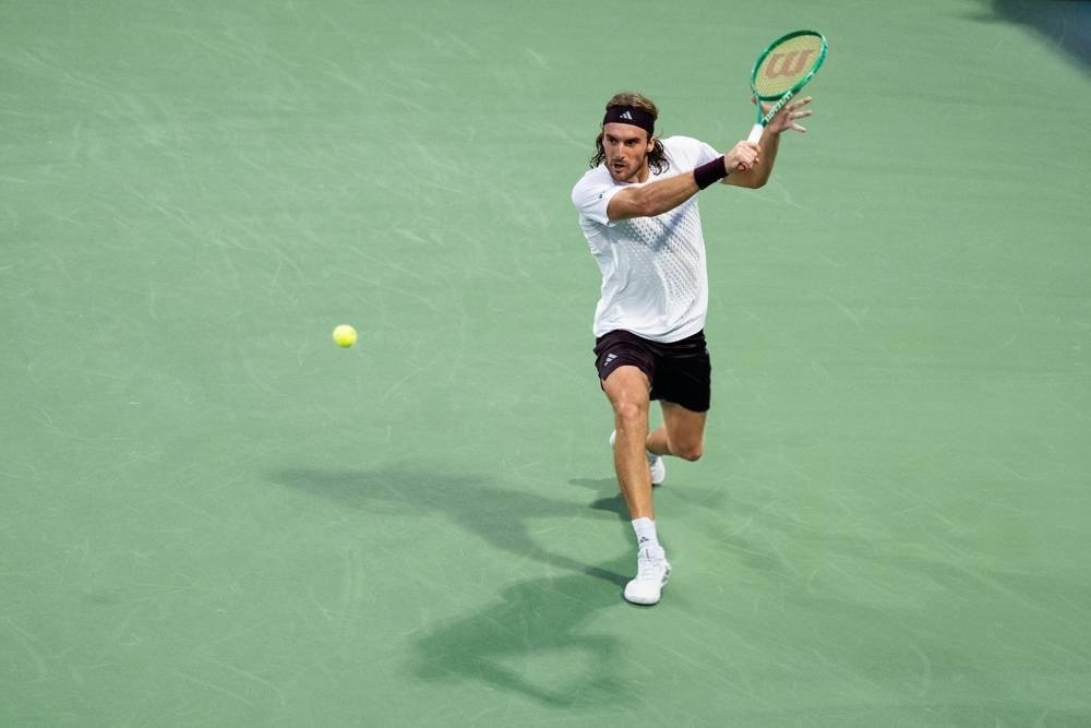 Tennis player in white shirt and black shorts, Wilson racket, hitting a forehand on a green court at the US Open.