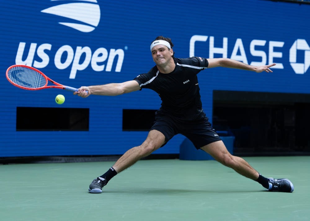 Tennis player in black BOSS shirt and white headband lunges to return a shot at the US Open, blue Chase backdrop