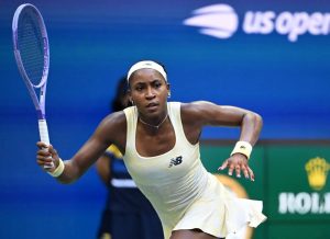 Tennis player in a white New Balance dress and headband swinging a purple racquet at the US Open, blue court backdrop