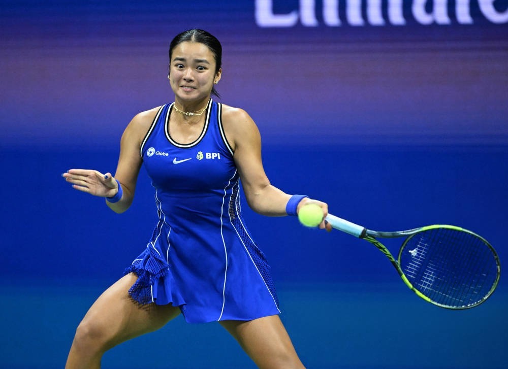 Tennis player in blue Nike dress with BPI and Globe logos hitting a forehand with a yellow-green racket at a US Open match.