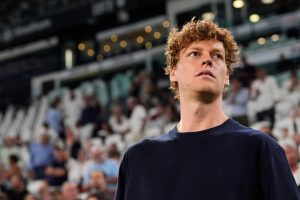A man with curly red hair in a navy shirt looks up in a stadium with blurred spectators behind him