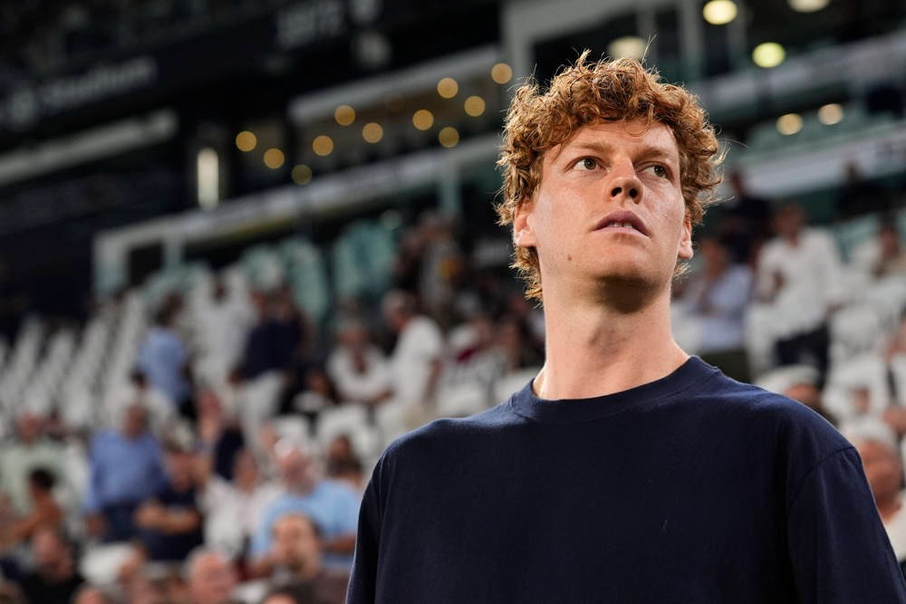 A man with curly red hair in a navy shirt looks up in a stadium with blurred spectators behind him