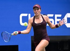 Tennis player in a maroon Adidas dress and visor swinging a forehand at the US Open, blue court backdrop with Chase logo