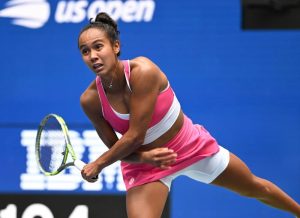 Leylah Fernandez serving in a pink top and skirt at the US Open, with a blue court backdrop behind her