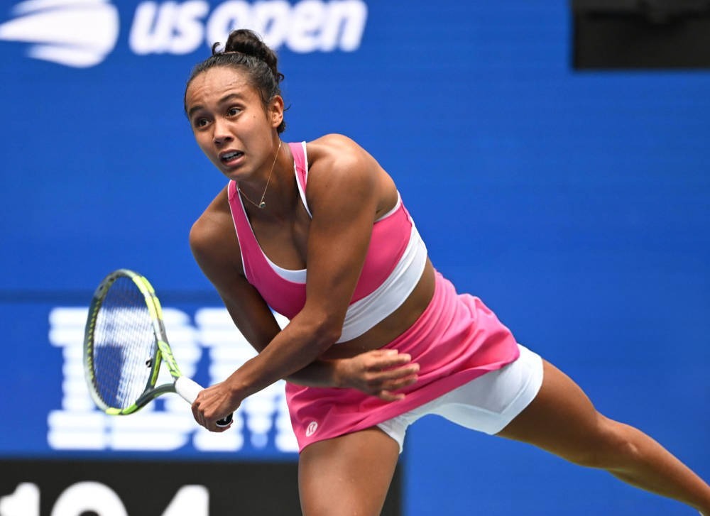 Leylah Fernandez serving in a pink top and skirt at the US Open, with a blue court backdrop behind her