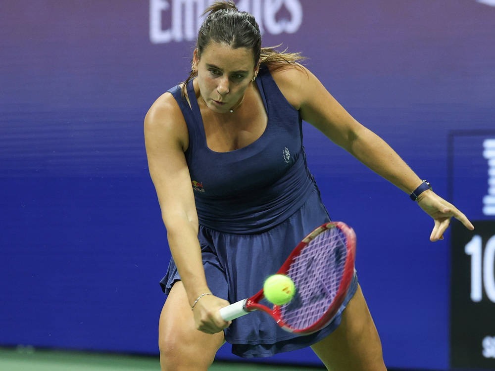 Tennis player in a navy dress hitting a forehand return at the US Open, with a red racket and a blurred blue backdrop