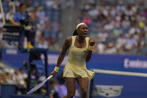 Tennis player in a pale yellow New Balance dress shouting and clenching her fist mid-match at the US Open, with a racket in hand