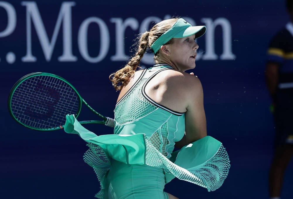 Tennis player in a mint-green Nike outfit and visor, hair in a braid, swinging a racket with a P. Morgan sign behind her at the US Open.