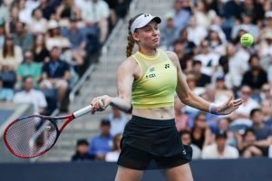 Tennis player in a yellow sleeveless top and black skirt, with a white visor and braid, hitting a forehand at the US Open.