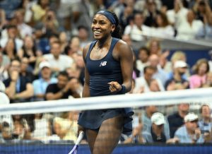 Tennis player in navy New Balance outfit and headband smiling on court at the US Open, crowd behind, with the article about Coco Gauff beating Iva Jovic.