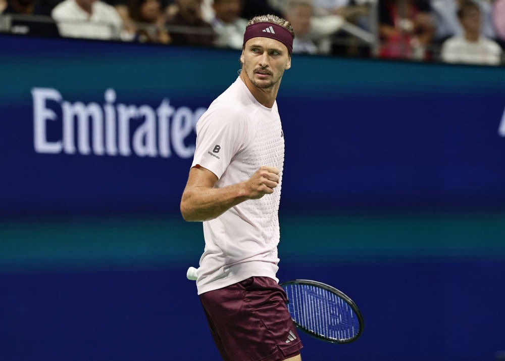 Tennis player in maroon headband and shorts, clenching fist and holding racquet on court at the US Open, Emirates sign behind him