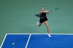 Tennis player in black outfit swinging a forehand on a blue hard court at the US Open, ball in the air.