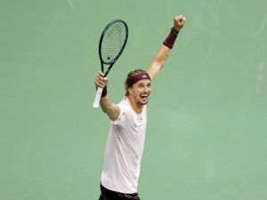 Tennis player in a white shirt and maroon headband, arms raised and fist clenched while holding a racquet on a green court, celebrating a US Open win