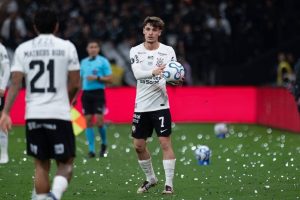 Breno Bidon in white Corinthians kit, number 7, holding a match ball on the pitch with confetti scattered on the grass.