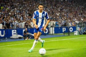 Football player in blue-and-white striped FC Porto kit dribbling the ball along the touchline in a packed stadium.