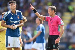 Jacobo Ramón in a blue Como jersey with arms clasped, while a pink-kitted referee points during a match
