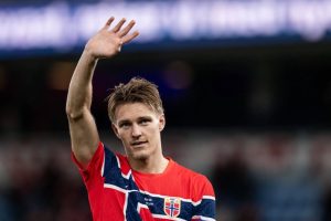 A footballer in a red and navy Norway national team shirt waves to the crowd in a stadium
