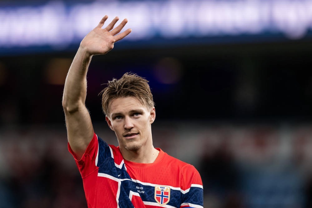A footballer in a red and navy Norway national team shirt waves to the crowd in a stadium