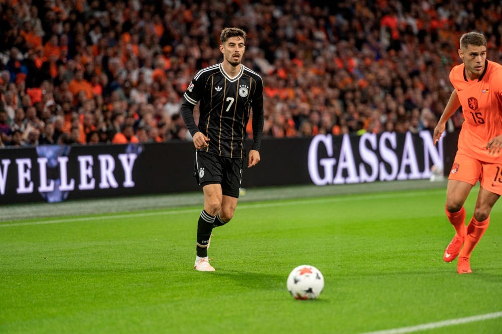 Footballer in black Germany kit, number 7, dribbling the ball on the pitch during a match against Netherlands in orange.