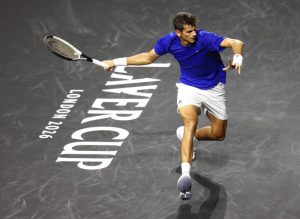 Tennis player in blue shirt and white shorts lunges to return a shot with a racket on a dark court marked "Laver Cup London 2026