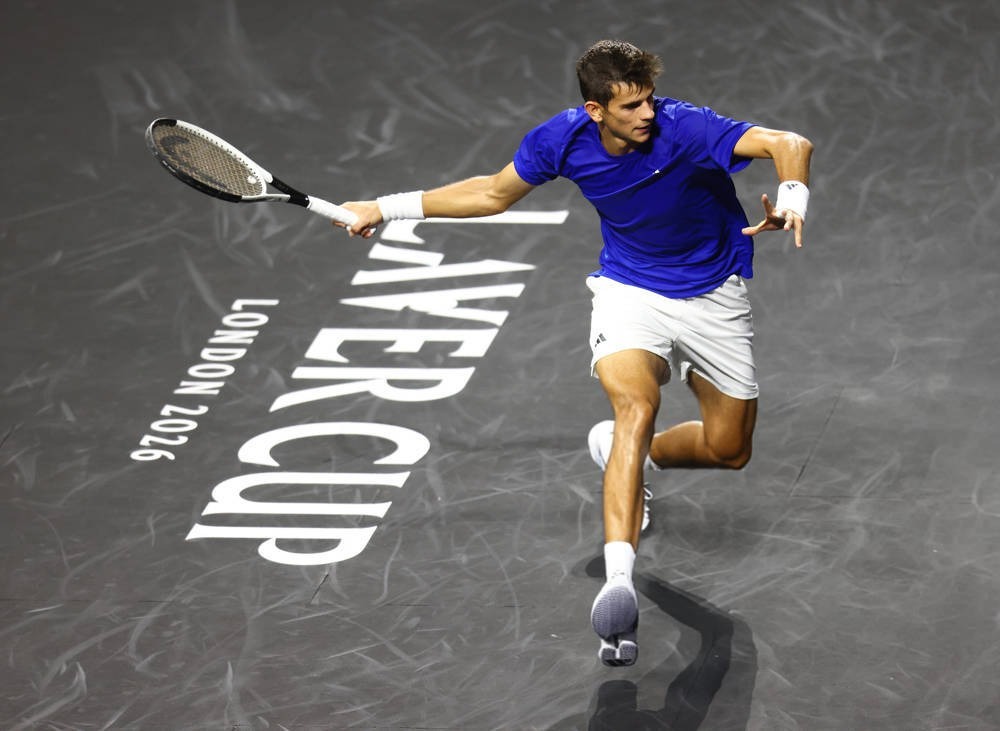 Tennis player in blue shirt and white shorts lunges to return a shot with a racket on a dark court marked "Laver Cup London 2026