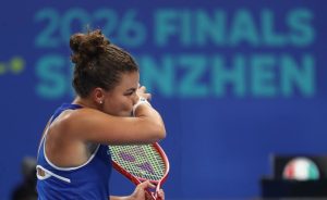Tennis player in blue top with a red-and-yellow racket covering her face at the 2026 Finals in Shenzhen, appearing dejected after a match.