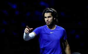 Tennis player in a blue Nike shirt and white arm sleeve pointing on a dark court, appearing to gesture during a Laver Cup match