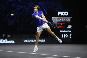 Tennis player in blue shirt and white shorts hits a forehand on court at the Laver Cup, with a 119 mph serve speed scoreboard behind him