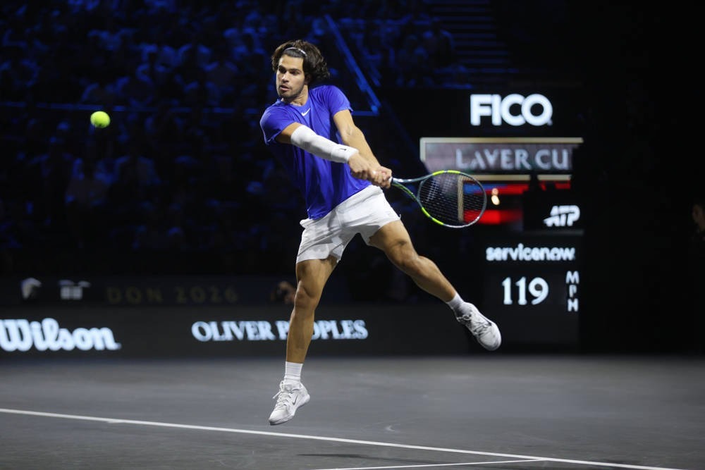 Tennis player in blue shirt and white shorts hits a forehand on court at the Laver Cup, with a 119 mph serve speed scoreboard behind him