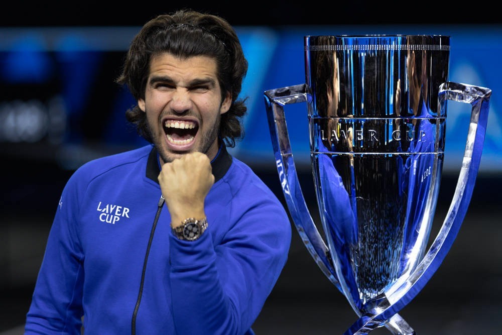 Man in a blue Laver Cup jacket clenching his fist and shouting in celebration beside the silver Laver Cup trophy