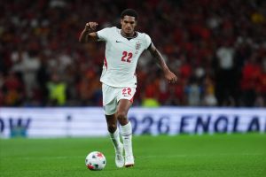 England defender in white number 22 kit dribbling the ball on the pitch during a night international match.