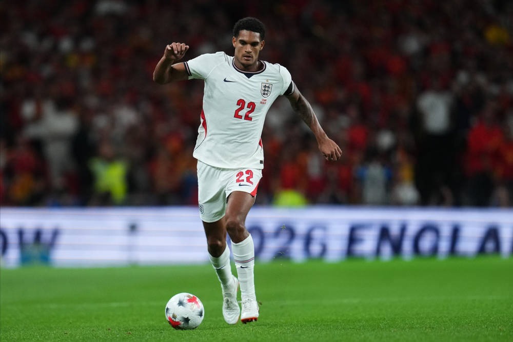 England defender in white number 22 kit dribbling the ball on the pitch during a night international match.