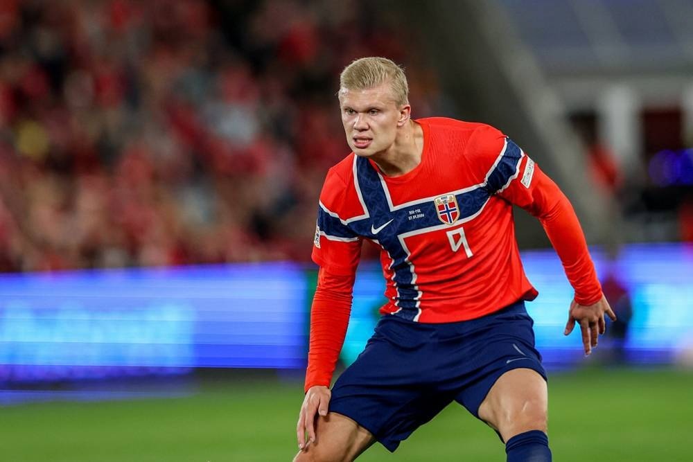 A footballer in a red and navy Norway national team kit with number 9 on the pitch during a match, looking intently ahead at a stadium.