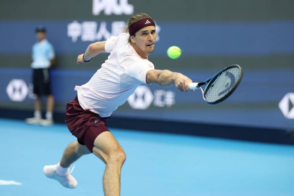 Alexander Zverev in a maroon headband and white shirt lunges to hit a forehand return at the China Open court.