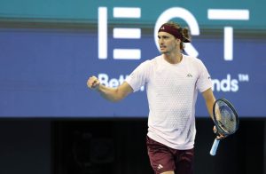 Alexander Zverev celebrates with a fist pump on court during a match, holding his racquet, with a sponsor backdrop behind him.