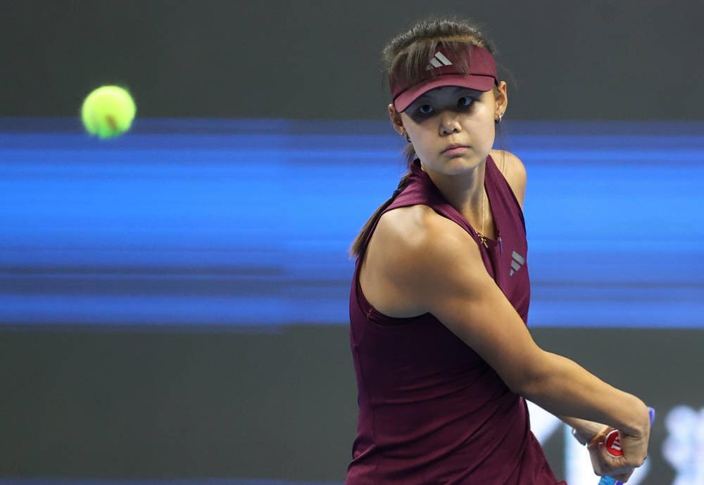 Tennis player in a maroon Adidas visor and sleeveless top hits a forehand on court at the China Open, ball in motion beside her.