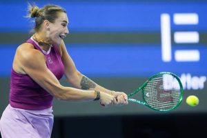 Aryna Sabalenka in a magenta top swinging a green Wilson racket at a tennis match, ball in flight, blue arena backdrop