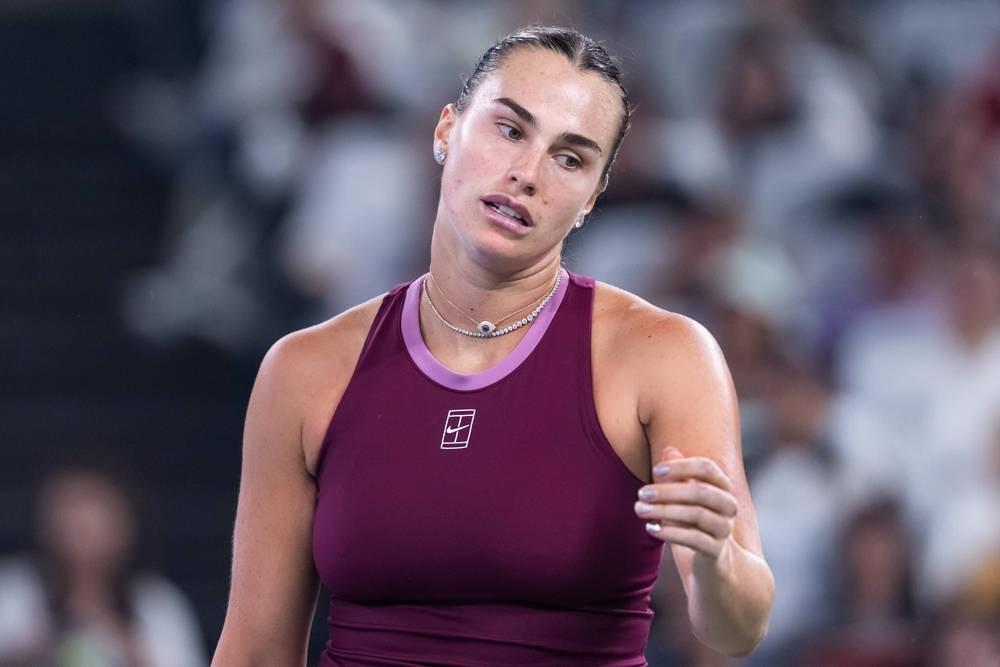 Aryna Sabalenka in a burgundy Nike tank top, grimacing and gesturing during a match at the Wuhan Open tennis tournament.
