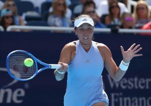Tennis player in light blue Adidas dress and white visor hits a forehand at a tournament with a crowd behind her