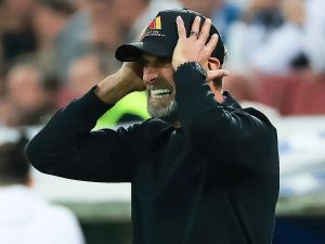 Man in black cap and sweatshirt, hands on head and grimacing in dismay at a stadium, crowd blurred behind him, matching the Germany Nations League defeat story