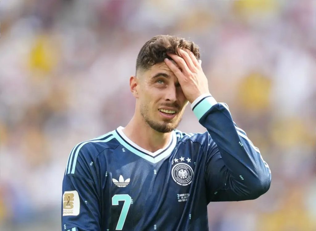 Footballer in navy Germany away kit, number 7, hand on head grimacing during a match, appearing to be Kai Havertz.