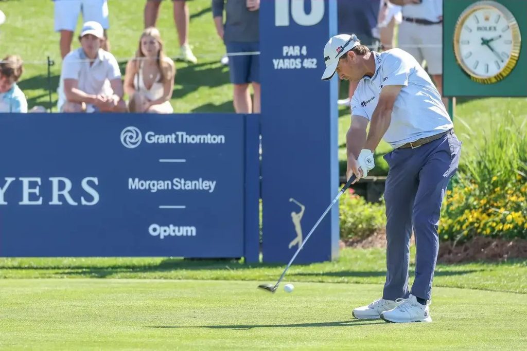 Golfer in white cap and polo swings iron on tee 16, par 4, 462 yards, with spectators and sponsor boards behind