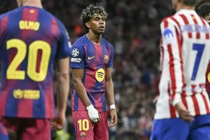 Barcelona player wearing number 10 jersey stands on the pitch with a bandaged hand, flanked by teammate Olmo (20) and an Atletico Madrid player.