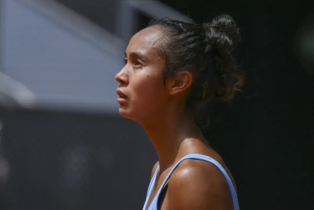Tennis player in a light blue top with hair in a bun, looking off to the side on a sunlit outdoor court at the Singapore Open.