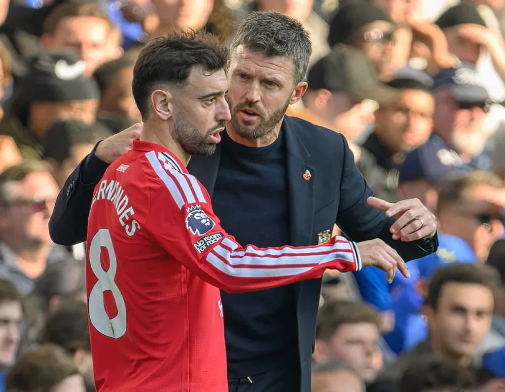 Jogador do Man United de vermelho, camisola 8 com o nome "Fernandes", fala com um treinador de fato escuro junto à linha, durante um jogo contra o Chelsea.