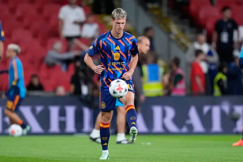 Dani Olmo in Spain kit warming up before a match, juggling a white ball on a pitch in a stadium.
